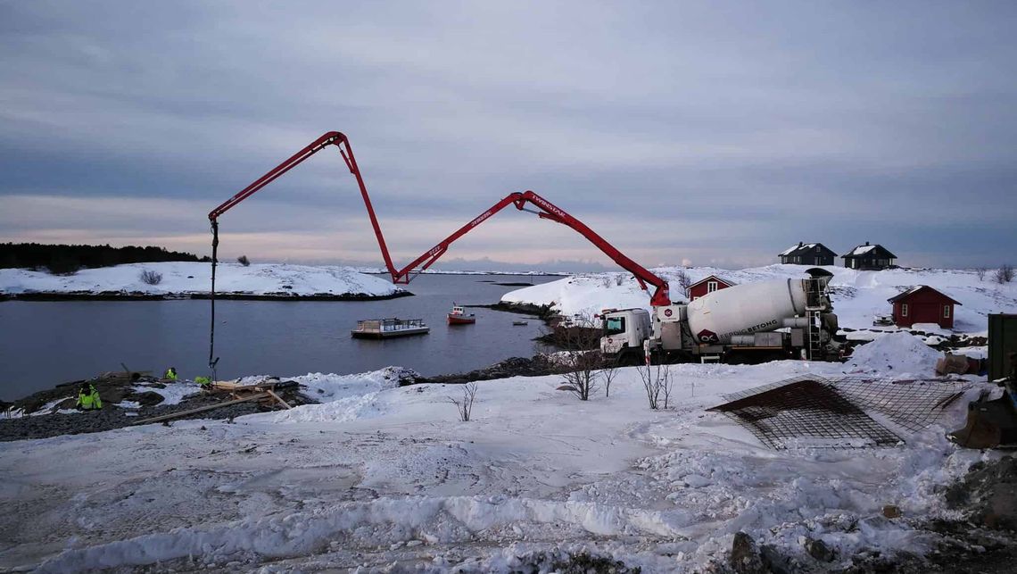 Betongbil med en lang kran ved en sjø